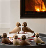 Sechs Holzvögel auf einem Tablett, vor einem Kaminfeuer.