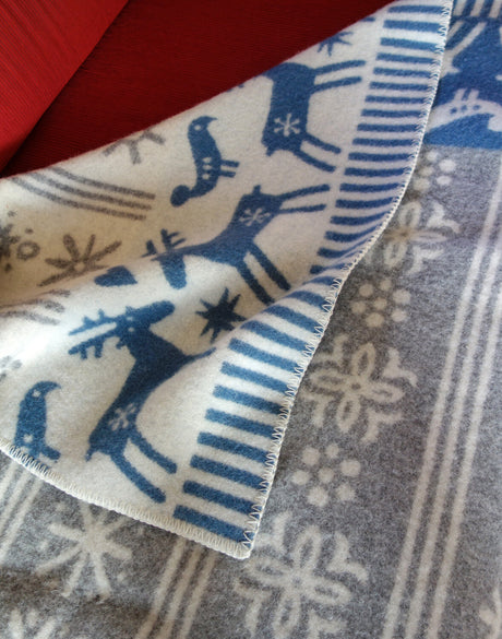 Blaue und weiße Weihnachtsdecke mit Rentieren, Schneeflocken und Sternen, auf grauem Weihnachtsmuster.