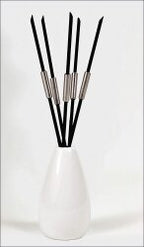Fünf schwarze Stäbchen mit silbernen Griffen in einer weißen Vase.