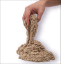Hand hält feuchten Sand, der nach unten rieselt, auf weißem Hintergrund.