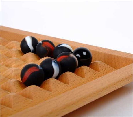 Holzspielzeug mit schwarzen, weißen und roten Kugeln in einer Vertiefung.