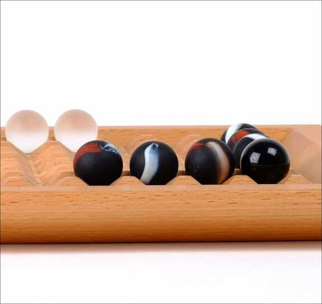 Zwei weiße und fünf schwarze Kugeln auf einem Holzspielbrett.