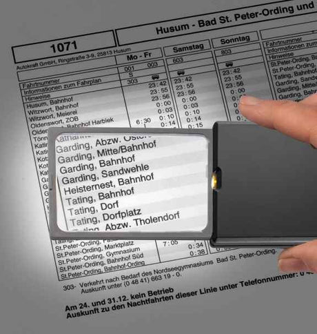 Hand hält Lupe über Fahrplan mit Haltestellen wie Garding, Tating und Heisternest.