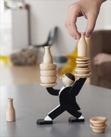 Hand legt Holzringe auf die Hände einer Figur, die wie ein Mensch in Anzug aussieht, auf einem Tisch.