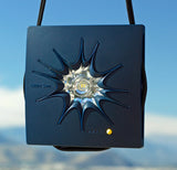 Kleiner, blauer Sonnen- oder Lichtprojektor mit schwarzem Band, auf blauem Himmel.
