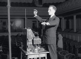 Mann in Anzug dirigiert ein elektronisches Orchester in einem Saal.