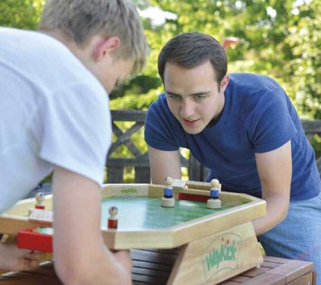 Zwei Männer spielen draußen auf einer Holzbank mit einem Wackel-Eishockeyspiel.