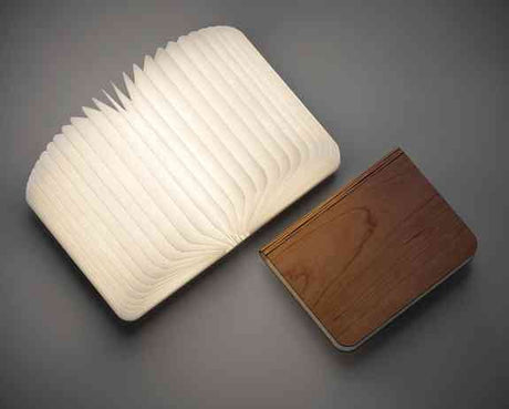 Ein Tischlampe mit einem weißen, gewellten Lampenschirm und ein gefalteter Holz- oder Holzoptik-Artikel daneben.