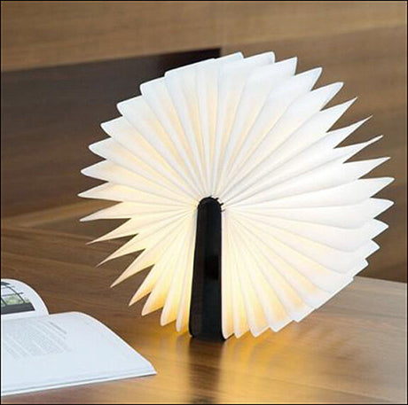 Leuchtendes, aufgeschlagenes Papierlampen-Design auf einem Tisch, neben einem offenen Buch.