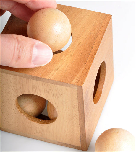 Hand hält Holzball über Holzspielzeug mit Loch, daneben weiterer Holzball.