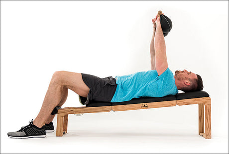 Mann liegt auf einer Bank, hebt ein Gewicht mit gestreckten Armen nach oben.