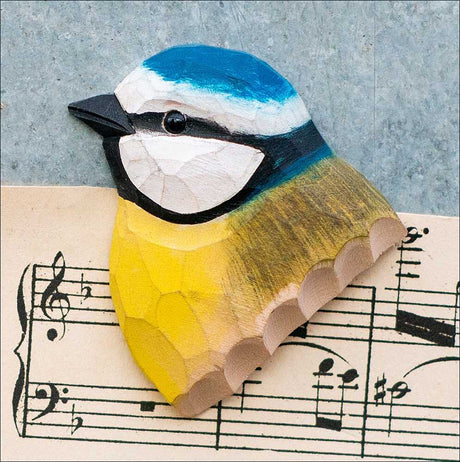 Holzschnitt eines bunten Vogelkopfs auf Notenblatt, mit blauer, weißer, schwarzer und gelber Farbgebung.