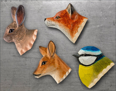 Vier handbemalte Holzmasken in Tierkopf-Form, darunter ein Hase, ein Fuchs, ein Reh und ein Vogel, auf grauem Hintergrund.