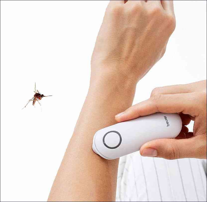 Person benutzt ein elektrisches Insektenstich-Entfernungsgerät am Arm, neben einer fliegenden Biene.