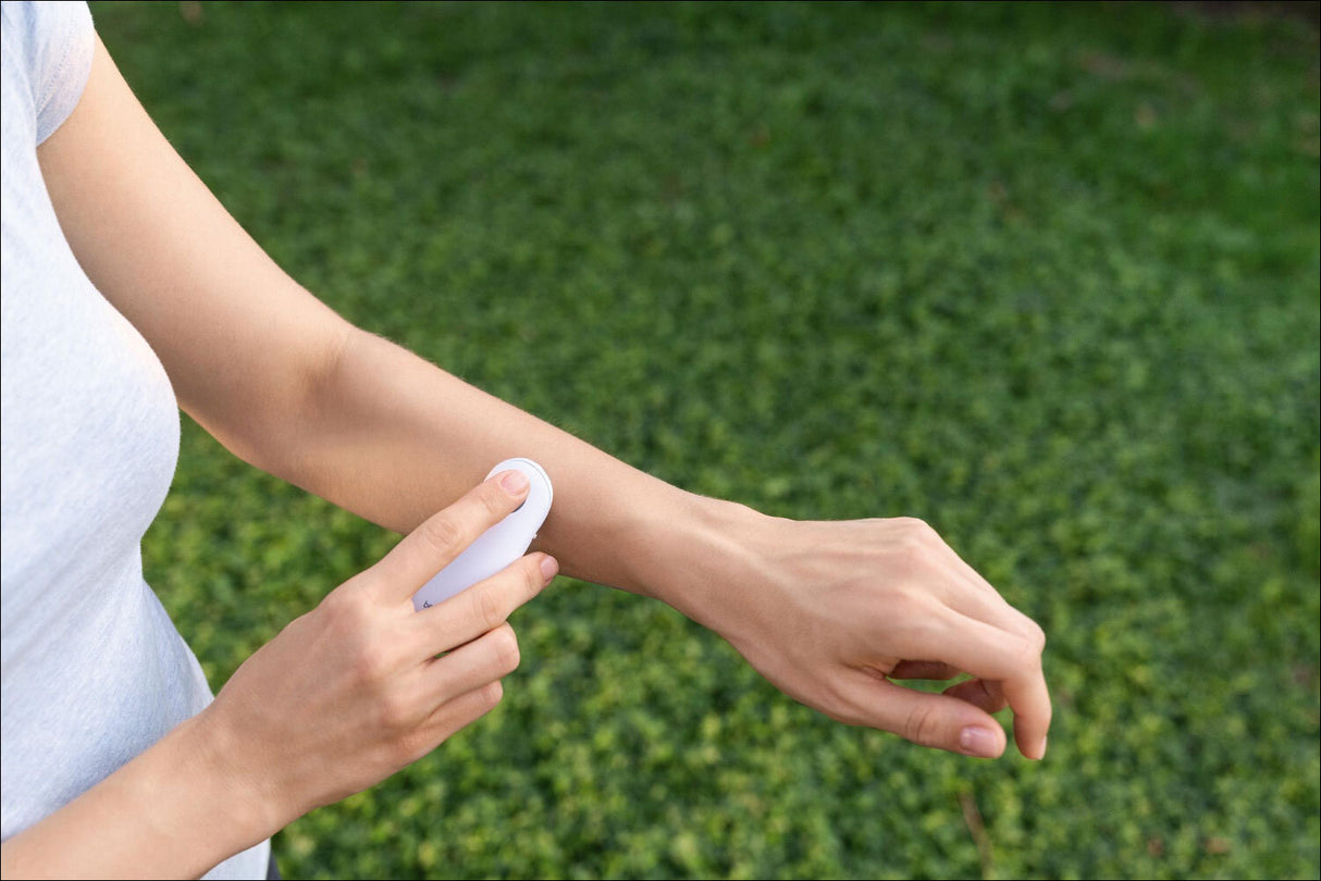 Person benutzt ein Handgerät zur Messung der Hauttemperatur am Unterarm, im Freien auf grünem Rasen.
