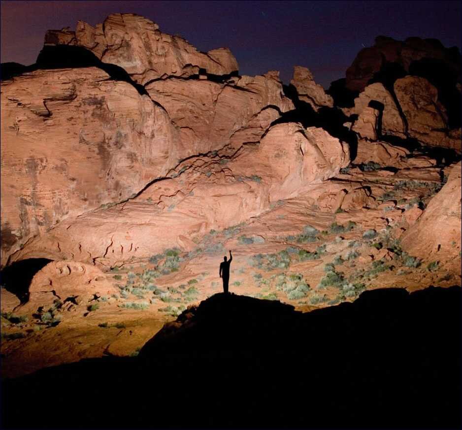 Ein Mensch steht auf einem Hügel vor einer großen Felswand bei Nacht, die im Mondlicht leuchtet.