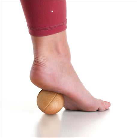 Fuß mit Holzball unter der Ferse, auf weißem Hintergrund, getragen von einer Person in rotem Sportshirt.