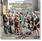 Kinder stehen mit Fahrrädern und Scooter vor einem Kiosk auf der Straße, einige schauen auf eine Werbetafel.