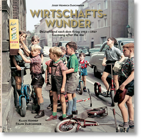 Kinder stehen mit Fahrrädern und Scooter vor einem Kiosk auf der Straße, einige schauen auf eine Werbetafel.