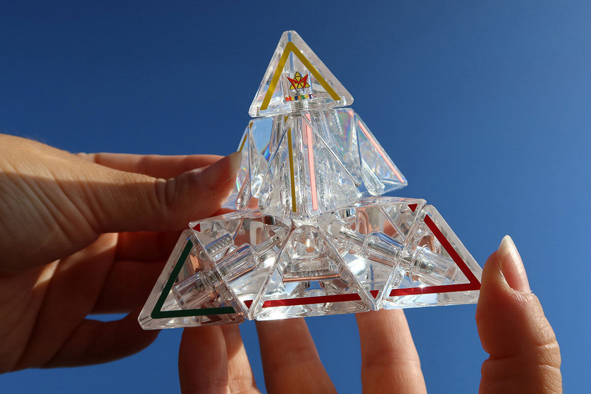 Transparenter, geometrischer Kristall mit bunten Linien, gehalten gegen blauen Himmel.