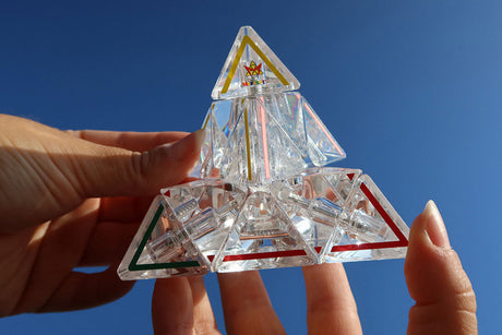 Transparenter, geometrischer Kristall mit bunten Linien, gehalten gegen blauen Himmel.