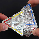 Hand hält einen transparenten, geometrischen Kristallwürfel mit farbigen Linien (rot, blau, gelb).