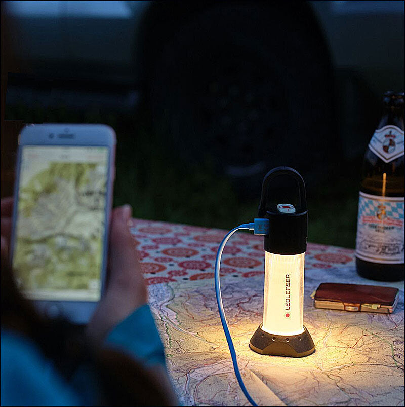 Tisch mit Karte, LED-Laterne, Smartphone, Bierflasche und Geldbörse bei Dämmerung.