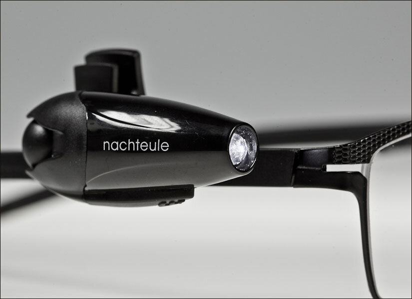 Schwarze Stirnlampe mit dem Schriftzug "nachtule" und einem LED-Licht, auf einer weißen Oberfläche.