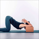 Frau in Yoga-Position, auf Knien, mit Kopf auf einem Block, Hände vor dem Gesicht, in einer entspannten Haltung.