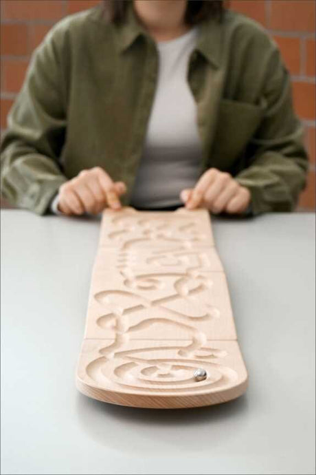 Person sitzt hinter Holzplatte mit eingravierten Buchstaben, die Platte liegt auf einem Tisch.