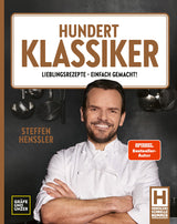 Buchcover mit einem lächelnden Koch in Weiß, hinter ihm schwarze Wand mit Kochutensilien, Titel "Hundert Klassiker"