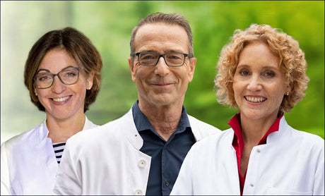 Drei Ärzte in weißen Kitteln vor grünem, unscharfem Hintergrund, lächelnd in die Kamera schauend.