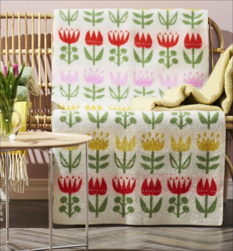 Bunte Handtücher mit Blumenmuster in Rot, Pink, Gelb und Grün auf einem Korbregal.