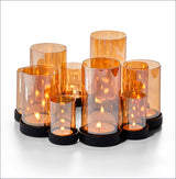 Mehrere brennende Kerzen in orange-transparenten Glasvasen auf schwarzem Untersetzer.