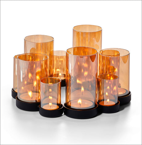 Mehrere brennende Kerzen in orange-transparenten Glasvasen auf schwarzem Untersetzer.