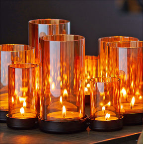 Mehrere brennende Kerzen in orangefarbenen Glasvasen auf einer schwarzen Oberfläche.