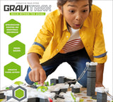 Junge spielt mit Gravitrax-Module, baut ein Kugelbahn-System, trägt gelbe Jacke und schaut gespannt.