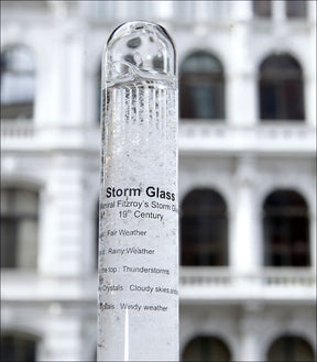 Ein Stormglas mit Wetterbeschreibung, vor einem Gebäude mit weißen Balkonen.