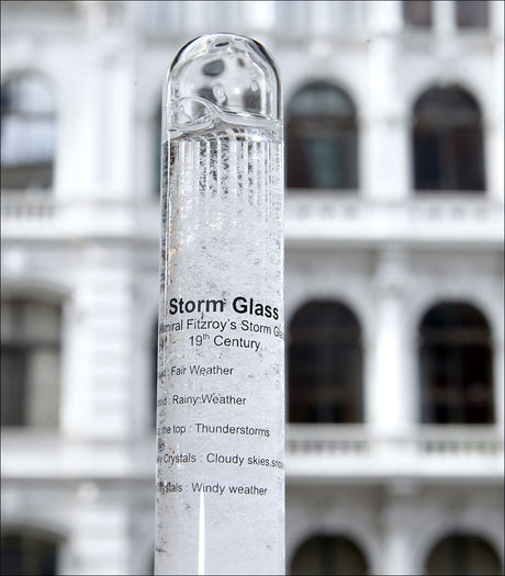 Ein Stormglas mit Wetterbeschreibung, vor einem Gebäude mit weißen Balkonen.