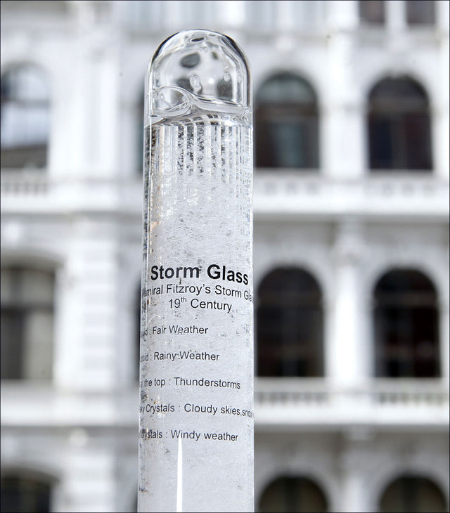 Ein Stormglas mit Wetterbeschreibung, vor einem Gebäude mit weißen Balkonen.