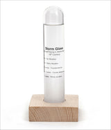 Klares Stormglas in einer Holzbasis, mit Textbeschreibung auf der Glasfläche.