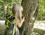 Mädchen mit Rucksack beobachtet Baum durch eine Lupe im Wald.
