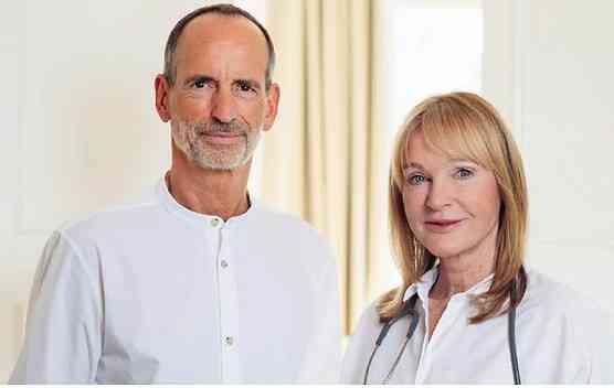 Ein Mann und eine Frau stehen nebeneinander in einem Raum mit natürlichem Licht, beide tragen weiße Oberteile.