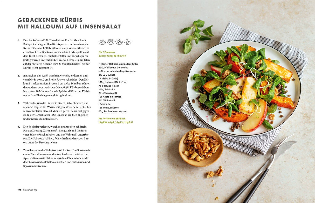 Bunter Salat mit gebackener Kürbis, Halloumi, Apfel, Walnüssen und Linsen auf einem weißen Teller, daneben eine kleine Schale mit 