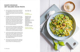 Bunter Zucchini-Nuss-Pesto-Zoodles auf einem weißen Teller mit geriebenem Käse, Nüssen und Selleriegrün.
