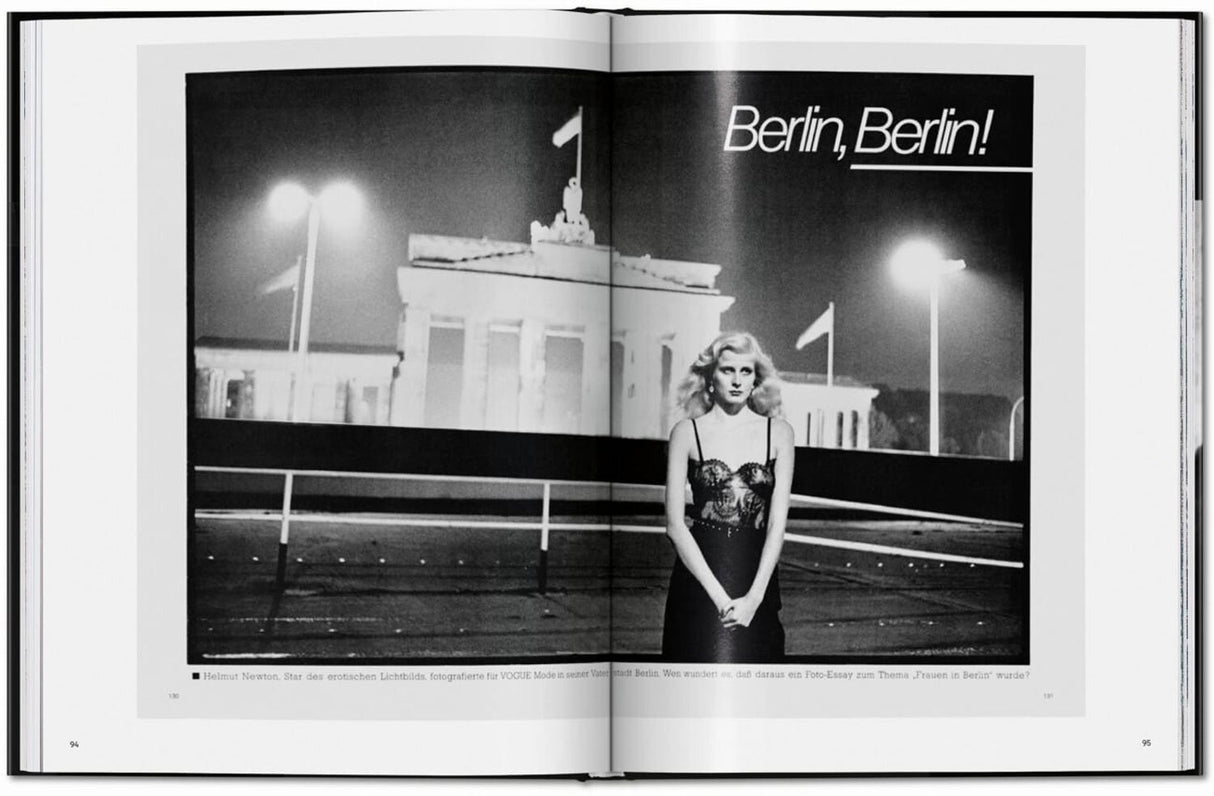 Schwarz-Weiß-Foto einer Frau in einem eleganten Kleid vor dem Brandenburger Tor in Berlin, nachts, mit Straßenlaternen.