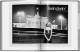 Schwarz-Weiß-Foto einer Frau in einem eleganten Kleid vor dem Brandenburger Tor in Berlin, nachts, mit Straßenlaternen.