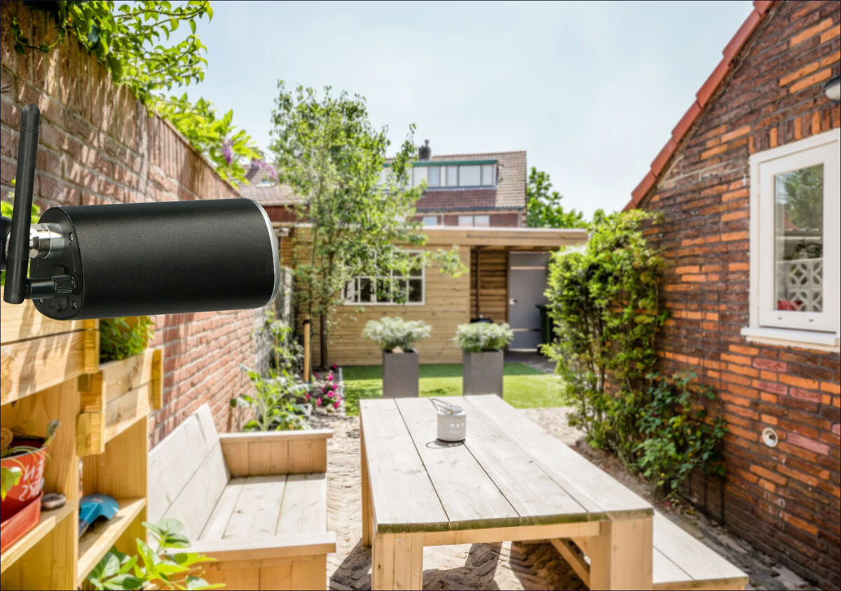 WLAN-Antenne an einer roten Backsteinmauer, Blick auf einen Garten mit Tisch, Bänken, Pflanzen und einem kleinen Holzhaus.