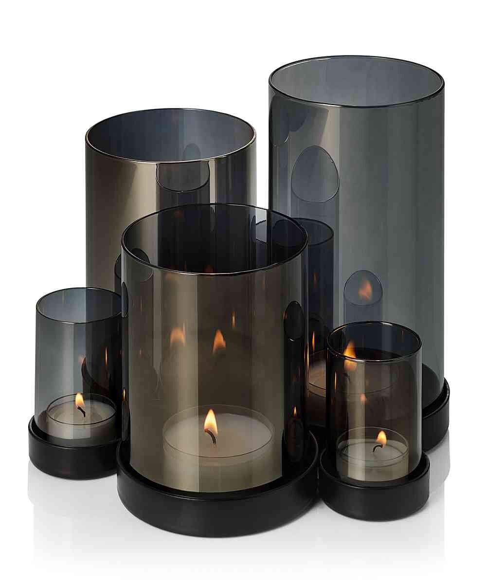 Fünf schwarze, transparente Kerzenhalter mit brennenden Kerzen in unterschiedlichen Größen.