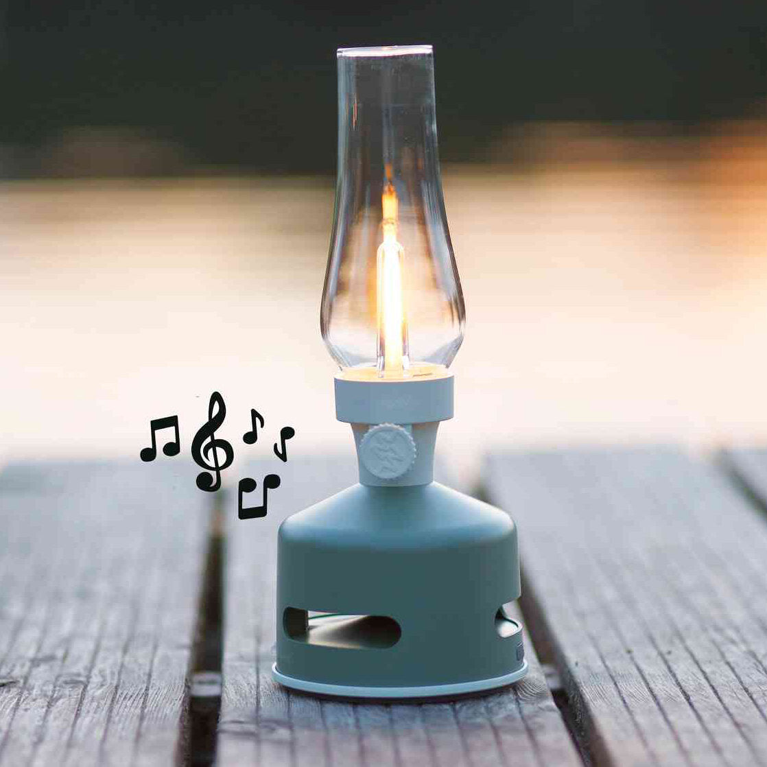 Ein batteriebetriebener Campingkocher mit einer glühenden Glühbirne, die wie eine Flamme aussieht, auf einer Holzoberfläche im Freien, mit musikalischen Noten daneben.